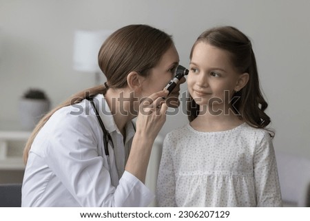 Female laryngologist in white coat using professional otoscope instrument examining little girl ear during her visit in clinic. Otolaryngology, children healthcare, inflammation infection prevention Royalty-Free Stock Photo #2306207129