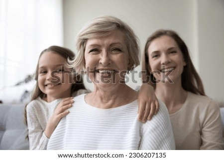 Attractive optimistic mature 60s woman looks at camera pose for picture with lovely granddaughter and young adult daughter. Caucasian female relatives feel happy, portrait of intergenerational family Royalty-Free Stock Photo #2306207135
