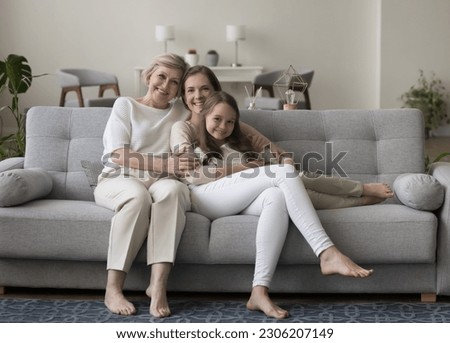 Beautiful diverse age and generation Caucasian women posing for camera seated on couch in living room, smile looking happy to spend time together, having good harmonic relations, feel warmth and bond