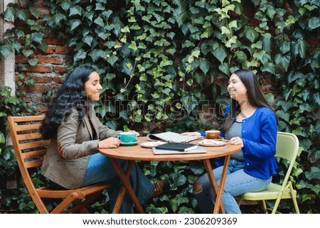 Friends and Coffee: Cafe Patio with lush foliage Hosts Two Young Latina Women Enjoying Coffee and Sweet Pastries
