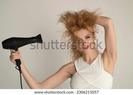 Young woman drying her hair with a hairdryer isolated on studio background. Young woman with blow dryer drying hair, making hairdo. Close up portrait of beautiful young woman in drying hairstyle. Royalty-Free Stock Photo #2306215057