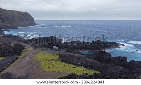 The rugged, black volcanic coastline of western Sao Miguel island, Azores is shown alongside turquoise waters of the Atlantic Ocean during the day.