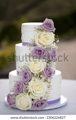 Three tiered wedding cake with lilac and cream roses and purple ribbon Royalty-Free Stock Photo #2306226827