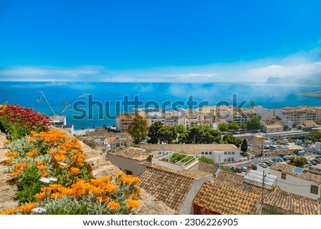 Landscape view photo of Altea Spain with bright orange flowers in the foreground bright blue sky Mediterranean sea and whispy clouds