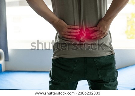 Unhappy young man in gray t-shirt suffering from severe back pain Touch your back to try to ease the pain in your spine. close up pictures