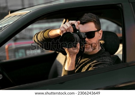 Man detective or agent taking photos from the car, wearing modern sunglasses  Royalty-Free Stock Photo #2306243649