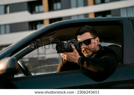Man detective or agent taking photos from the car, wearing modern sunglasses  Royalty-Free Stock Photo #2306243651