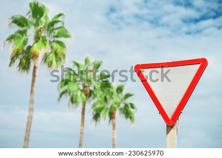 "Give way"' sign against palms and sky.