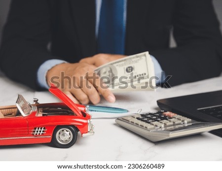 Car loan or Title loan. US dollar bills in a hand businessman while sitting at the table. Miniature a red car model, a calculator, and a laptop on a table. Car finance and insurance concept Royalty-Free Stock Photo #2306260489
