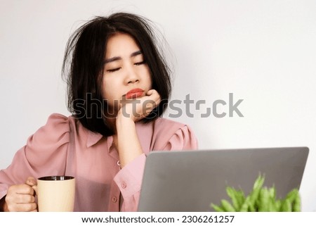 Asian woman Feeling tired or lacking energy after waking up and not feeling refreshed to start the day at the workplace hand holding a glass of coffee at the office desk  Royalty-Free Stock Photo #2306261257