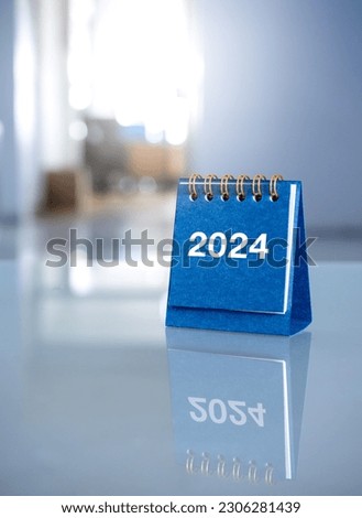 Happy new year 2024 background. 2024 numbers year on blue small desk calendar cover standing on glass table at office workplace with copy space, vertical style. Business goals and success concepts.