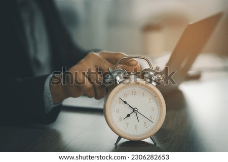 Selective focus of alarm clock on desk near business man using laptop to working overtime for deadline at home, concept of time management. business concept.