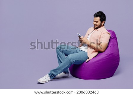 Full body young Indian man he wear pink shirt white t-shirt casual clothes use mobile cell phone surfing internet isolated on plain pastel light purple background studio portrait. Lifestyle concept