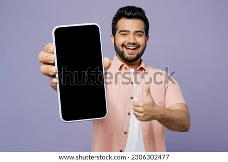 Young Indian man wears pink shirt white t-shirt casual clothes hold in hand use close up mobile cell phone with blank screen workspace show thumb up isolated on plain pastel light purple background Royalty-Free Stock Photo #2306302477