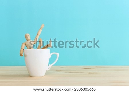 Funny picture of a wooden figure jumping into a cup of coffee