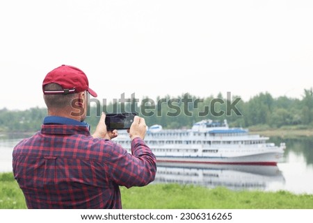 A man takes pictures on a smartphone of a passenger ship sailing on the river. People and technology. Summer navigation.