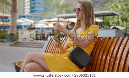 Young woman in dress trying to open bottle with green smoothie in the park. 