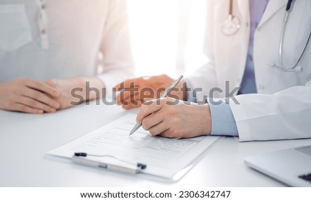 Doctor and patient discussing current health questions while sitting near of each other and using clipboard at the table in clinic, just hands closeup. Medicine concept. Royalty-Free Stock Photo #2306342747