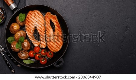 Grilled salmon steaks and potatoes sizzling in a frying pan, a mouthwatering delight. Flat lay with copy space Royalty-Free Stock Photo #2306344907