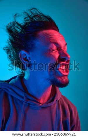 Funny portita of man posing with wind blowing into face against blue studio background in neon light. Concept of human emotions, facial expression, lifestyle. Meme look Royalty-Free Stock Photo #2306369921