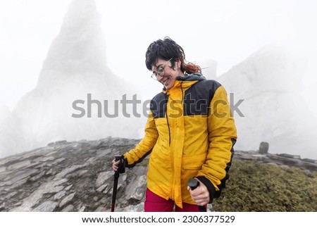 woman on the mountain in the fog with rain, wet, long hair looking for cover with cell phone, wild scene, taking pictures in nature, high mountains in the background