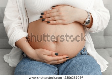 Cropped image pregnant woman sitting in appartment strokes hugging the belly tummy abdomen enjoying pregnancy. Future family, baby infant expecting child inside
