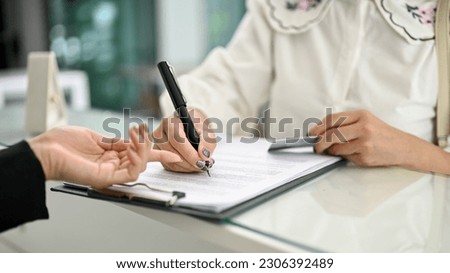 Close-up image of a customer filling out a form and signing her signature on a document at the hotel lobby.