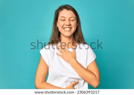A young caucasian woman isolated laughs happily and has fun keeping hands on stomach.