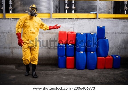 Portrait of chemical worker in protection suit and gas mask standing in factory and showing dangerous material. Royalty-Free Stock Photo #2306406973