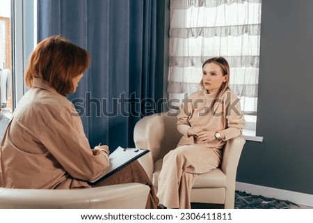 Young woman talking about her mental health problems. Two positive confident diverse business colleagues women talking at workplace, discussing project documents. Mature manager consulting expert. Royalty-Free Stock Photo #2306411811