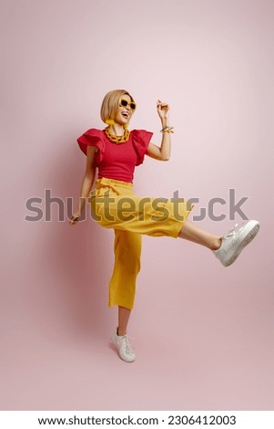 Full length of excited young woman in vibrant clothes dancing against colored background Royalty-Free Stock Photo #2306412003