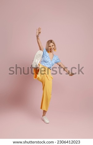 Full length of playful young woman in trendy clothes kicking and smiling against color background