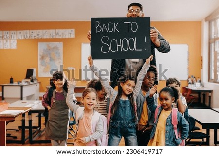 Teacher and students holding up a back to school sign in a classroom. Elementary class is excited to return to school and enter a new grade. Back to school celebration in primary school.