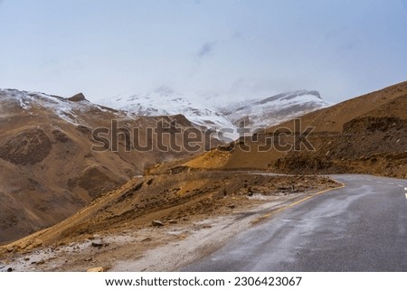 Snow covered mountains, cloudy sky, the road at Tanglang La Pass, elevation 5,328 metres (17,480 ft), is a high altitude mountain pass in the Indian union territory of Ladakh.  Royalty-Free Stock Photo #2306423067
