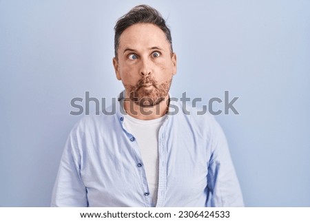 Middle age caucasian man standing over blue background making fish face with lips, crazy and comical gesture. funny expression. 