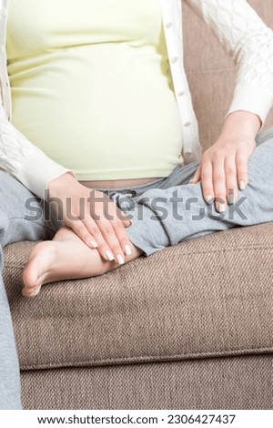 Leg cramps during pregnancy. Closeup of hands massaging swollen foot while sitting on sofa.
