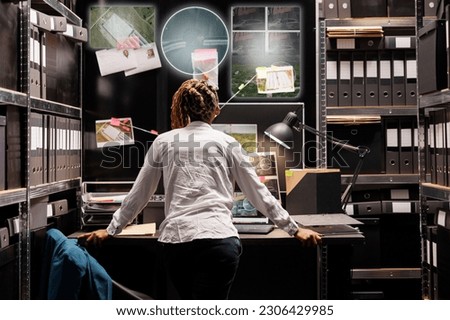 Young detective looking at hologram in incident room, trying to solve felony with evidence and insight. Private investigator examining holographic images with artificial intelligence at desk. Royalty-Free Stock Photo #2306429985