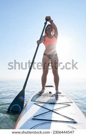 Portrait of sportswoman floating on paddle surf against of blue sky.Backlit
