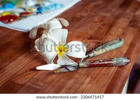 Two palette knifes n wooden table with white frangipani flowers Royalty-Free Stock Photo #2306471417