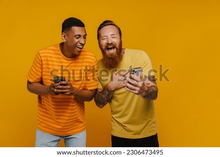 Two excited men laughing while looking at phone screen standing isolated over the orange background Royalty-Free Stock Photo #2306473495