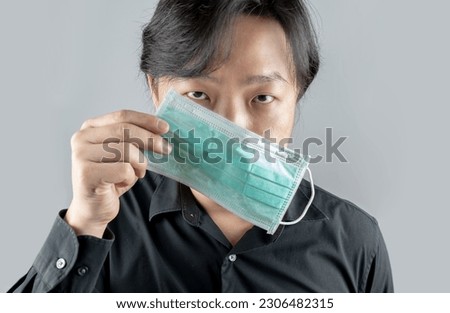 Asian middle man in a black shirt, wears a green hygienic mask, and crosses his arm backside, stands in front of a white clear background.