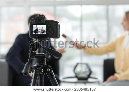 Female journalist with microphone having an interview with man on camera screen in office, closeup Royalty-Free Stock Photo #2306485159