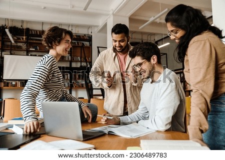 Group of young cheerful multinational students in casual wear having discussion while studying in college library Royalty-Free Stock Photo #2306489783