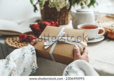 The child's hands hold a beautiful gift box with a ribbon against the backdrop of a festive breakfast. Top view, close-up. Happy mother's day.