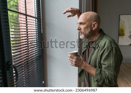 Man with introverted tendencies finds solace and tranquility in his apartment. Positioned near a window, he gazes outward, lost in thought and contemplation. . High quality photo