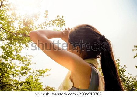 Back view Asian woman doing sport jogging feeling sun and heat too hot during jogging in park sweltering summer weather covering face with hands covering face against UV rays. Royalty-Free Stock Photo #2306513789
