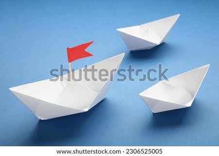 White paper ship and red flag on blue background. Top view