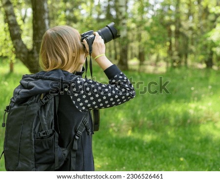 A woman with a backpack taking a picture with a digital camera during a trip to the forest