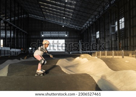 asian child surf skater or kid girl fun playing skateboard or ride surfskate in indoor pump track in skate park by extreme sports surfing to wears helmet elbow pads wrist knee support for body safety Royalty-Free Stock Photo #2306527461