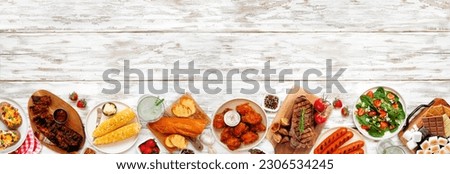 Summer BBQ food bottom border over a white wood banner background. Assortment of grilled meats, potatoes, vegetable dishes and smores platter. Top view with copy space.